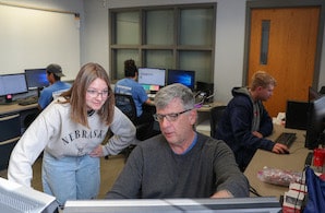  Benson works with a student in UNK’s Supply Chain Center. Students can use workspaces and equipment to participate in virtual internships during the academic year./></div><figcaption class=