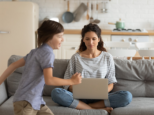 mother on laptop with son running by