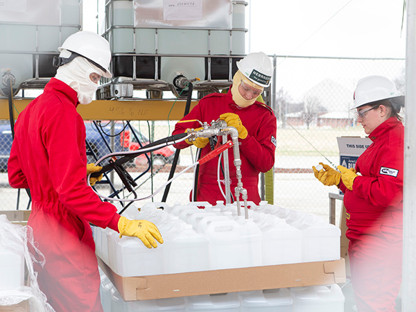 Hand sanitizer is mixed and loaded into jugs inside a fenced off section of the Food Innovation Center parking lot